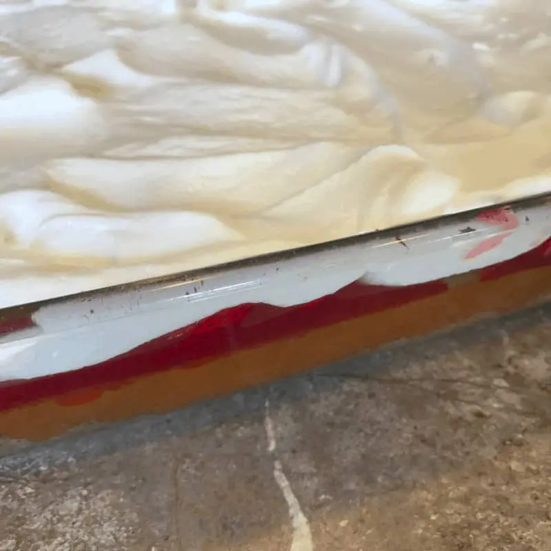 A close of of a baking dish with strawberry cheesecake bars topped with cool whip in it.