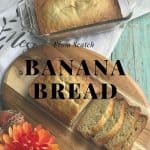 Banana bread in a load pan that is on a white towel. On a wooden cutting board is another banana bread loaf that has been sliced. In the bottom left corner is a orange flower. The words From Scratch Banana Bread is in the middle of the picture.