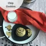 In the background is a jar with cookies in it. There is a white tray that has an orange napkin on it with a grey plate that has chocolate chip cookies on it. There is also a glass with milk on the tray. In front of the tray is chocolate chips.