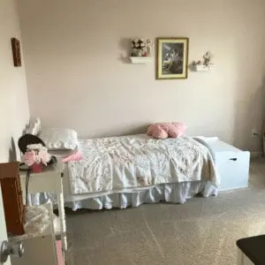 Bed with pink pillow on it, night stand and picture on the wall.