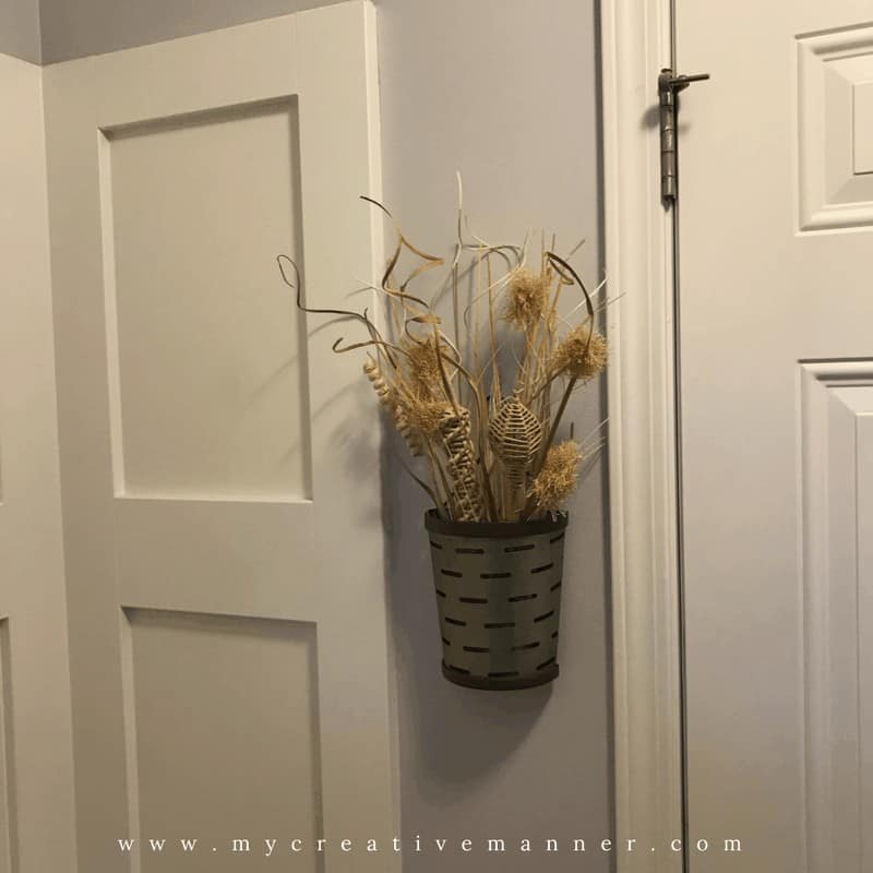 Metal planter hanging on a wall with grasses in it. 