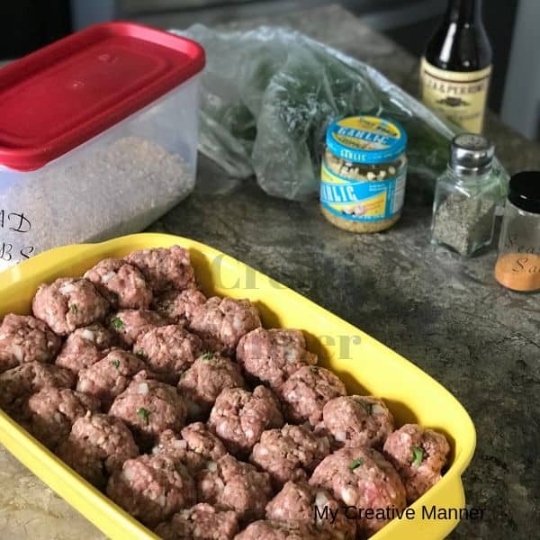 Bread crumbs in the background with a baking dish that has raw meatballs in it.
