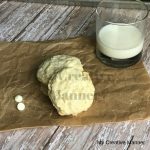 Amazing White Chocolate Coconut Cookies on a brown paper with a glass of milk next to it.