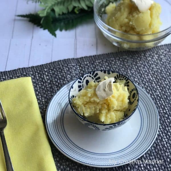 Bowl with mashed potatoes in it and a yellow napkin next to it. There is another bowl in the back ground filled with mashed potatoes.
