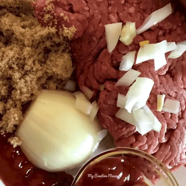 raw ground beef, onion, brown sugar, and ketchup on a plate.
