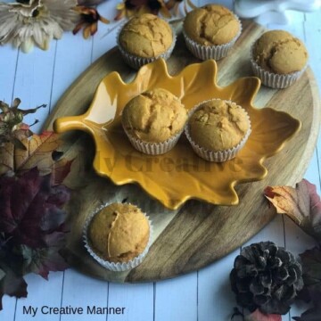 Wood tray with pumpkin muffins on it and leaves and a pumpkin around the wood tray.