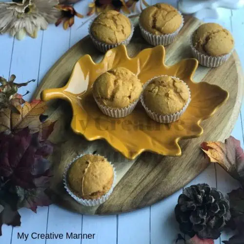 Wood tray with pumpkin muffins on it and leaves and a pumpkin around the wood tray.