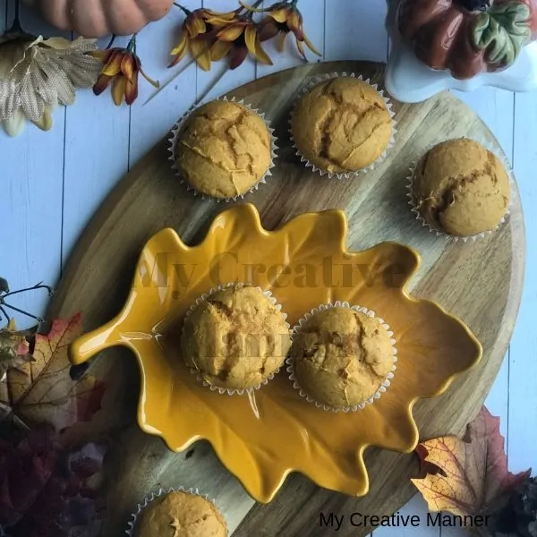 Wood tray with pumpkin muffins on it and leaves and a pumpkin around the wood tray.