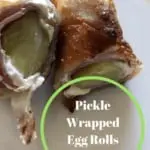 Pickle wrapped in cream cheese and ham that is wrapped in an egg roll wrapper that has been deep fried and cut in half. Then placed on a white plate.