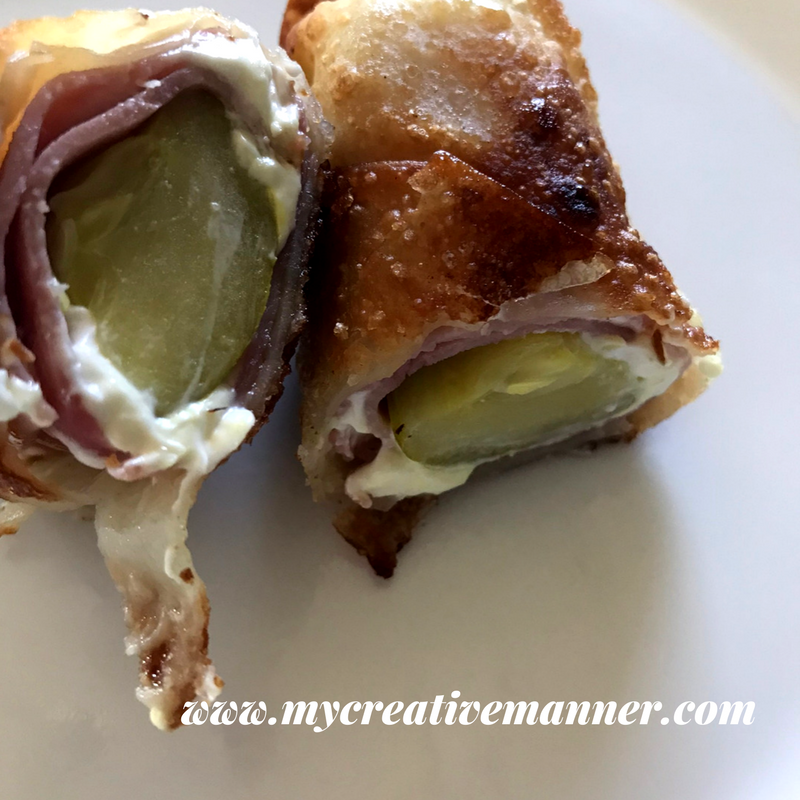 White plate that has a Pickle wrapped egg roll that has been cut in half.