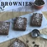 Three Killer Fudge Brownies on a plate with measuring spoons in front of the plate. On the brown paper is another killer fudge brownie and chocolate chips. Behind the plate is a measuring cup full of chocolate chips and a towel. The words Killer Fudge Brownies are at the top of the picture.