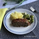 Blue plate mat with a a plate that has The Best Ever Meatloaf , mashed potatoes, and broccoli on it. There is a yellow napkin on the left of the plate while on the right is a fork.