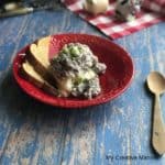 Red bowl with hamburger gravy over mashed potatoes in it with two slices of toast next to it.There is a wooden spoon next to the bowl. Behind the bow is a red and white napkin.