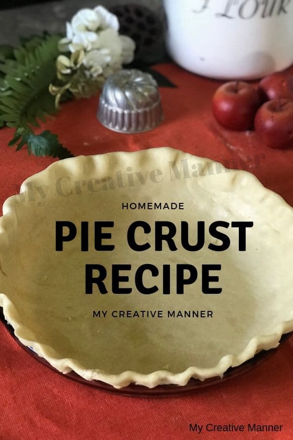 A pie crust that is in a pie dish that has not been baked. There is apples and a flour container in the back ground.