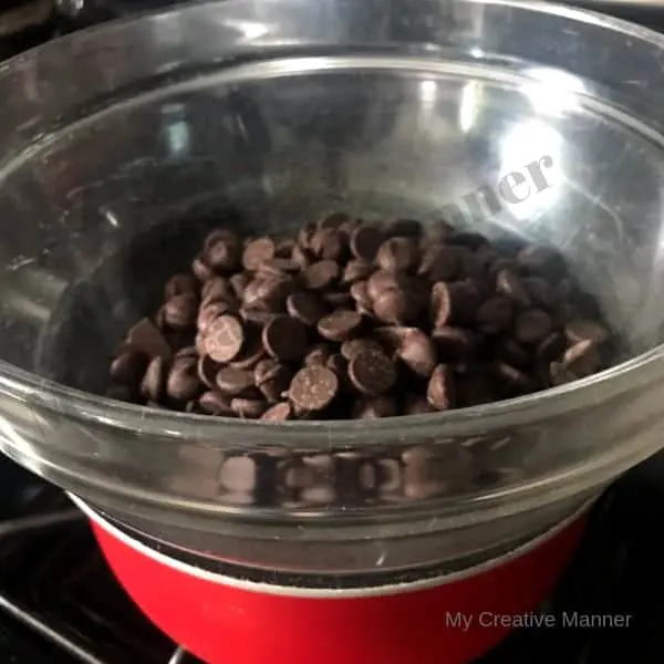 A sauce pan that has a clear bowl in it and the bowl has chocolate chips in it. 