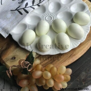 White platter with hard boiled eggs on it. That is sitting on a wooden cutting board with grapes in front of it.