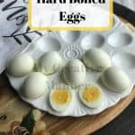 White platter with hard boiled eggs on it. That is sitting on a wooden cutting board with grapes in front of it. With the words Instant Pot Hard Boiled Eggs at the top of the picture.