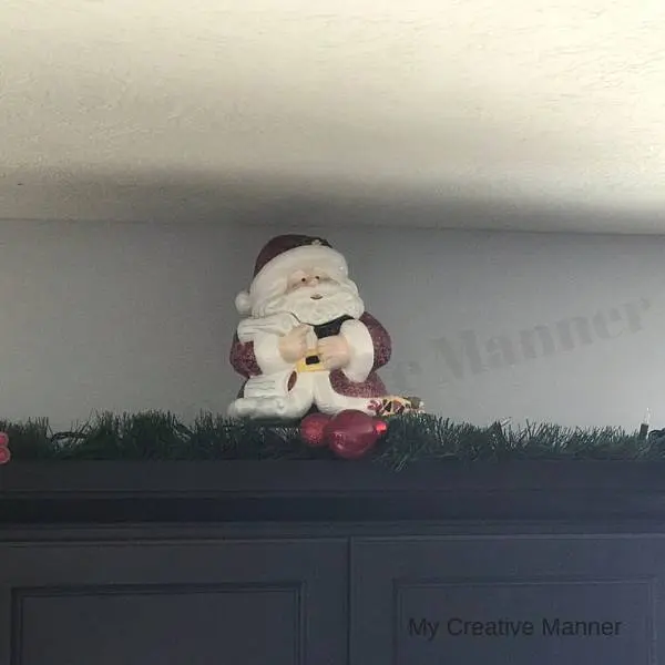 Santa Claus Cookie Jar sitting on top of a cupboard with green garland around it.