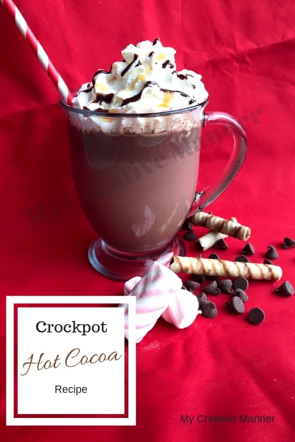 clear glass that has hot cocoa in it with whipped cream on top and a straw sticking out. Marshmallows, chocolate chips, and cookies lay in from on the cup.