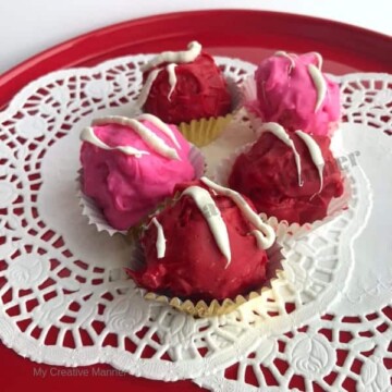 Strawberry cake balls that have been coated in chocolate in a cake stand.
