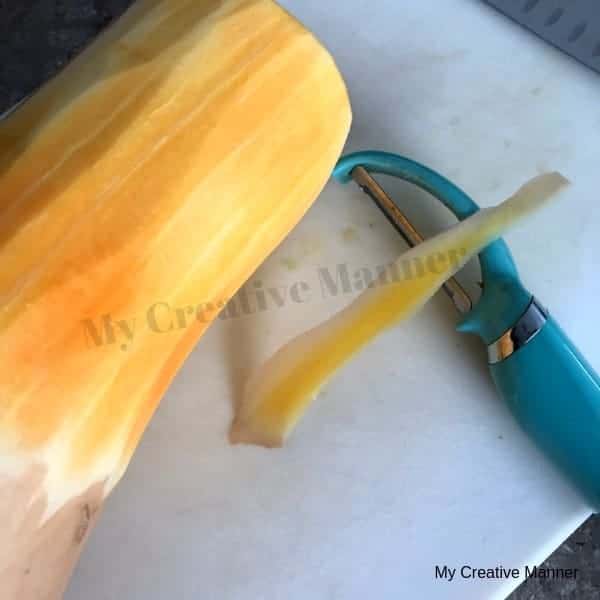 Cutting board with a peeled butter nut squash and vegetable peeler on it. 