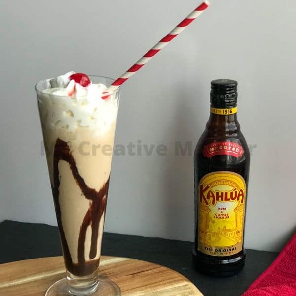 A tall glass that is full of frozen mudslide cocktail with a bottle of Kahlua next to it.