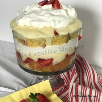 Glass trifle bowl layered with yellow cake, strawberries, cheesecake pudding, and cool whip.