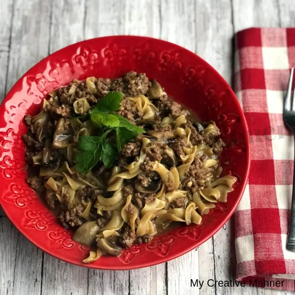 Red bowl filled with Hamburger Helper Beef Pasta with a red and white napkin next to the bowl with a fork on the napkin.