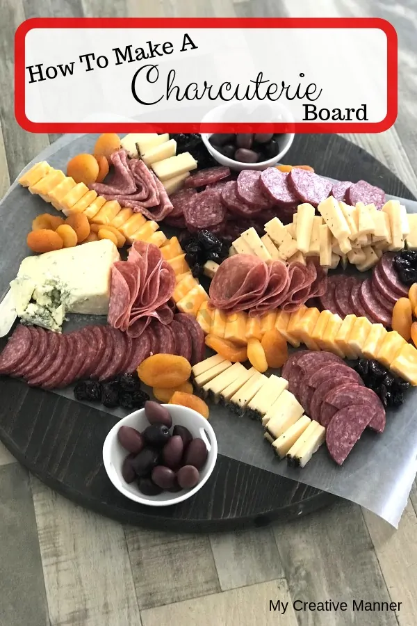 Round board with meats, cheese, dried fruit, and olives on it.