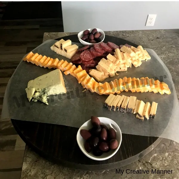 Round board with meats, cheese, dried fruit, and olives on it.
