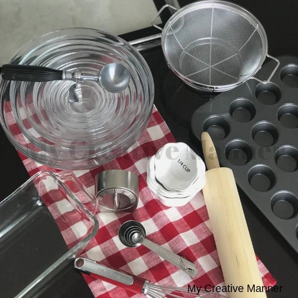 Glass nesting bowls, measuring spoons, measuring cups, rolling pin, muffin pan all sitting on a red and white napkin.