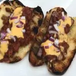 White plate with two Grilled hot Dogs that are in buns and topped with cheese, chili, and red onion.