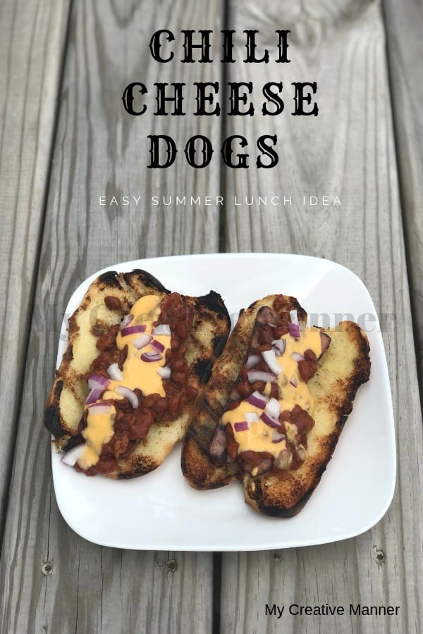 White plate with two Grilled hot Dogs that are in buns and topped with cheese, chili, and red onion. Chili Cheese Dogs Easy Summer Lunch Idea is at the top of the picture.