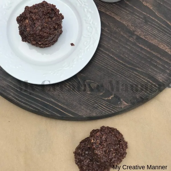 No bake cookies sitting on brown paper and two sitting on a white plate. The whit plate is sitting on a round piece of wood.