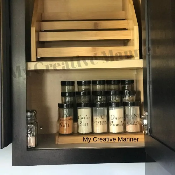 A cupboard that has a spice rack on the top shelf that is empty. The bottom shelf has a spice rack that is filled with spices.