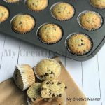 Muffin tin with Chocolate Chip Banana Bread Muffins in it. In front of the pan is three muffins on a brown paper. One of the muffins is cut in half.