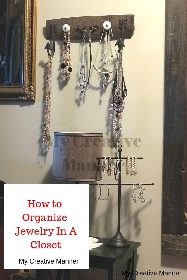 A table that has a lamp and a jewelry tree on it. On the wall is a full length mirror and a jewelry organizer.