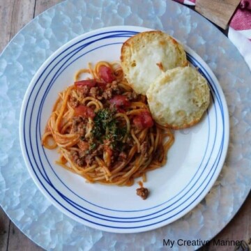 White and blue plate with Instant Pot spaghetti and rolls on it sitting on a silver plate charger.