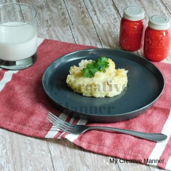 Grey plate with loaded mashed potatoes on it. Red salt and pepper shakers are behind the plate. The plate is sitting on a red and white napkin with a glass of milk .
