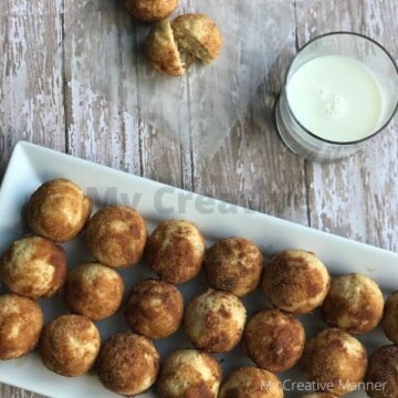 Long white plate filled with Cinnamon Sugar Mini Muffins. Behind the plate is two muffins and a glass of milk.