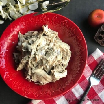 Red bowl filled with shredded chicken that was made in the Instant Pot or crockpot.. There is a red and white napkin in from of the bowl with a fork on it.
