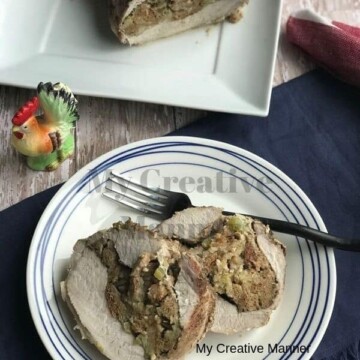 Round white plate with blue around the edge. On the plate is two pieces of stuffed pork loin and a fork. Behind the round plate is a square plate with the rest of the pork loin on it.