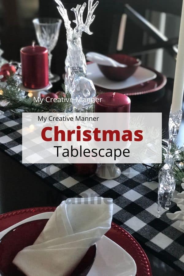 Black and white table runner with clear glass Christmas decorations and red candles. Red charger plates with a white plate and red bowl on them. There is a white napkin in each red bowl. Crystal glasses and silverware adron each place setting. With the words Christmas Tablescape in a white box over the image.