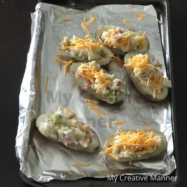 Foil lined cookie sheet with baked potatoes that have been cut in half and loaded with filling on it.