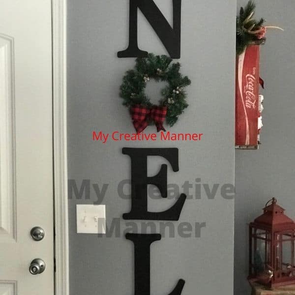 A wall that has letters that read Noel. The o in noel is made of a wreath.