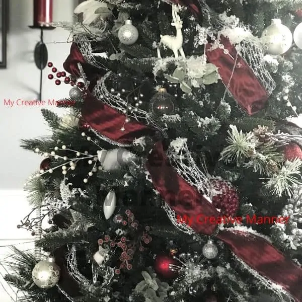 A close up of a Christmas tree that has red and silver ribbon on it.