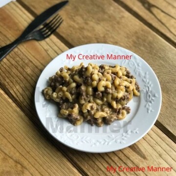 A white plate that has cheeseburger macaroni on it. Next to the plate is a fork and a knife.