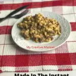 A white plate that is on a red and white placemat that has Cheeseburger Mac and Cheese on it. The words Cheeseburger Macaroni at the top of the image and Made In The Instant Pot at the bottom of the image.
