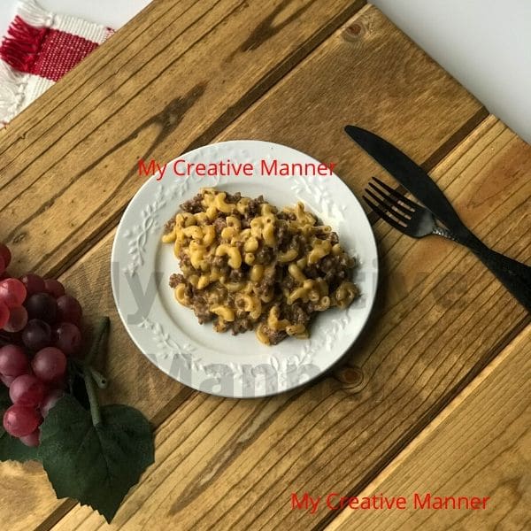 A white plate that has cheeseburger macaroni on it. Next to one side of the plate is a fork and a knife. On the other side is grapes.
