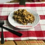 A white plate that has cheeseburger macaroni that was made in an Instant Pot on it. The plate is sitting on a red and white placemat. Next to the plate is a fork and knife.